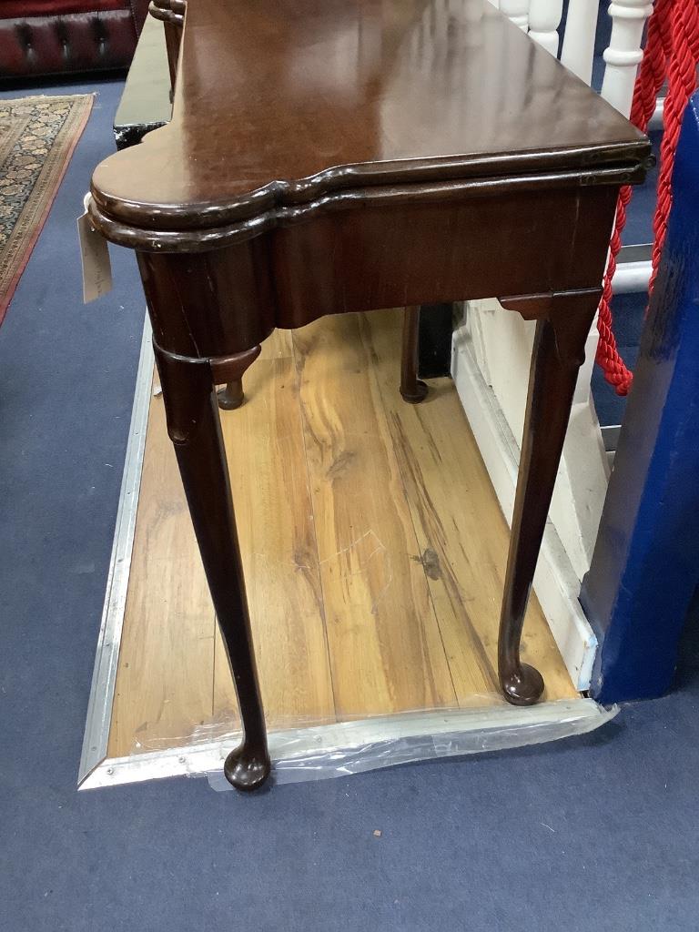 An 18th century mahogany games table, having shaped folding top enclosing counter wells and leather-lined surface on lappet-carved legs and pad feet, width 86cm depth 42cm height 72cm